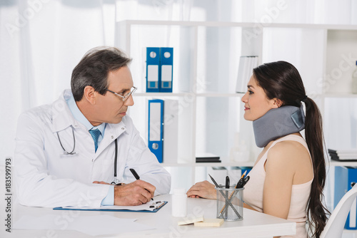 doctor sitting and talking with female patient in neck brace