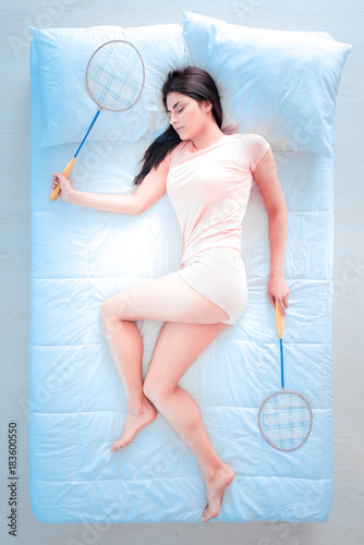 My equipment. Young woman keeping badminton rackets in both hands and lying on the side while dreaming about game