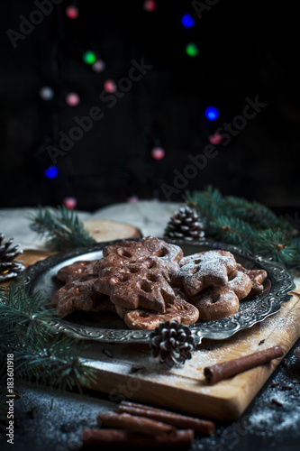 gingerbread cookies for the new year on a silver tray, New Year's lights, fireworks, fur-tree, cones, cinnamon on a wooden cutting board on a dark background