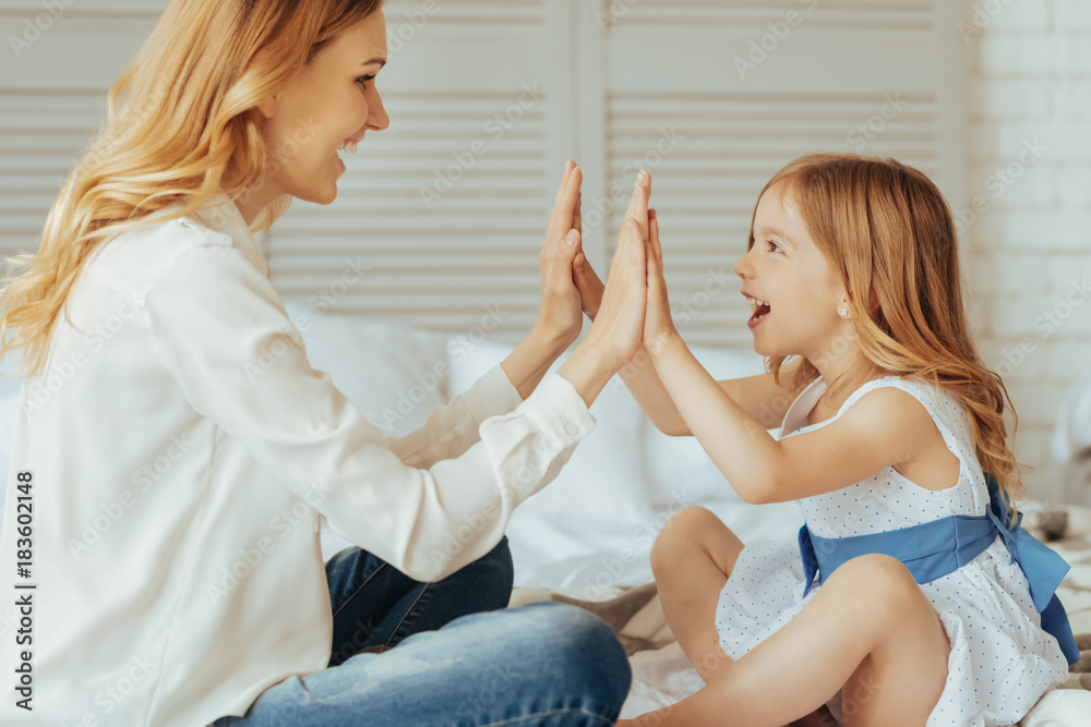 Pleasurable entertainment. Joyful nice delighted mother and daughter sitting opposite each other and laughing while playing a clapping game Pleasurable entertainment. Joyful nice delighted mother and daughter sitting opposite each other and laughing while playing a clapping game