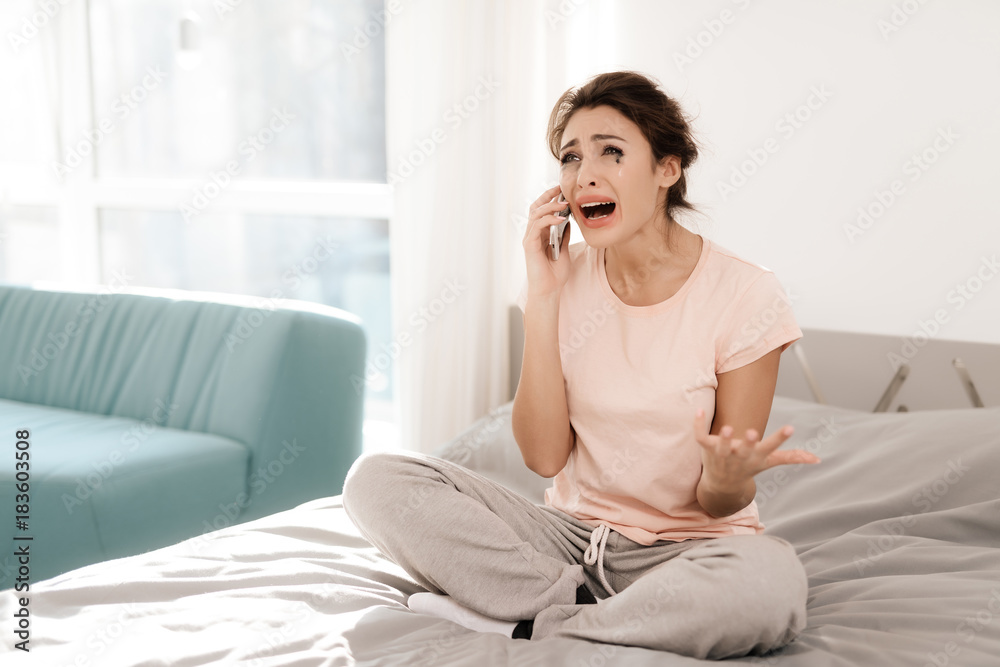 A lonely woman is crying alone, her mascara has flowed. She sits on a bed in a bright room. A lonely woman is crying alone, her mascara has flowed. She sits on a bed in a bright room.