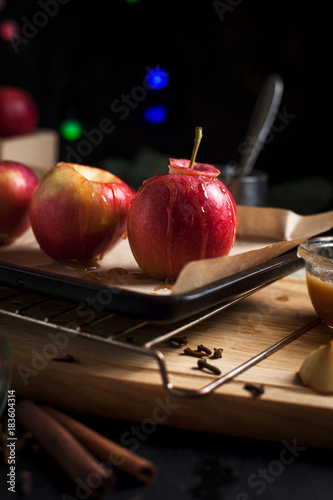 cooking of baked apples for New Year's holidays, Christmas tree and New Year's lights, honey and cinnamon on a wooden cutting board on a dark background