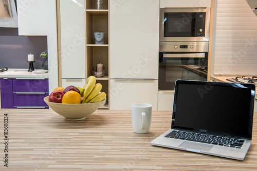 cozy modern kitchen interior with laptop and fruits in bowl photo