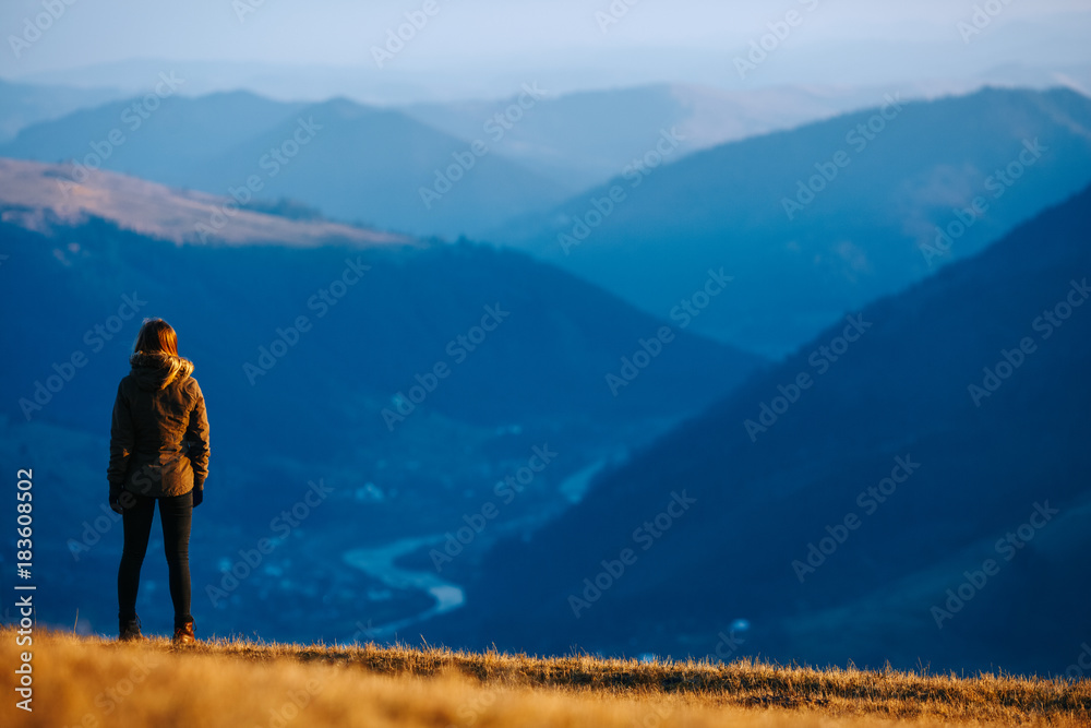 Young woman hiker hiking on mountain trail. Travel concept with space for text. Traveler standing on top of a mountain and enjoying sunset view