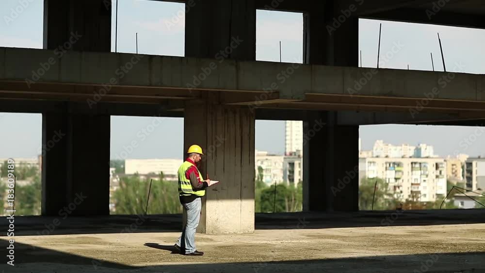 Worker at construction site. Building inspector with construction documentation at project site, builder write notes
