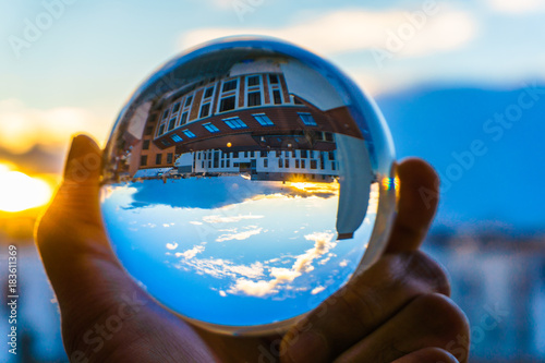 A hand holding a crystal ball for optical illusion. City as the background. Known as an orbuculum, is a crystal or glass ball and common fortune telling object. Performance of clairvoyance and scrying