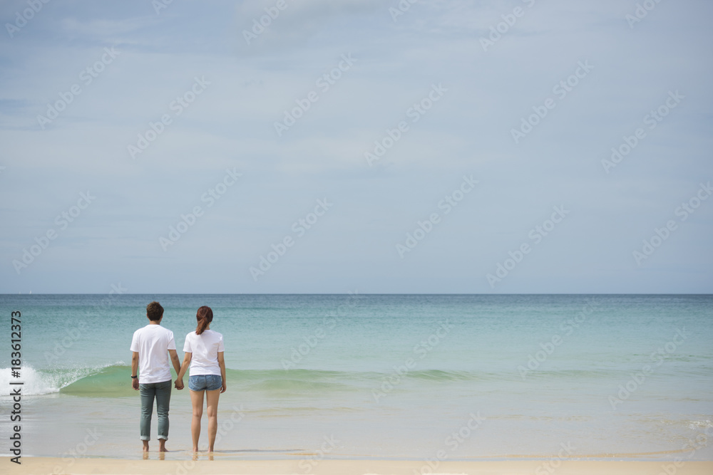 Young asian couple hold hand together stand on beach look to the sea on sunny day Young asian couple hold hand together stand on beach look to the sea on sunny day