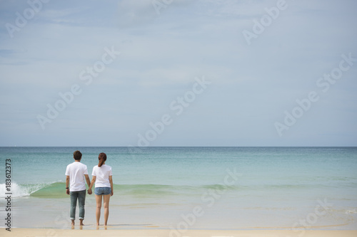 Young asian couple hold hand together stand on beach look to the sea on sunny day © mkitina4