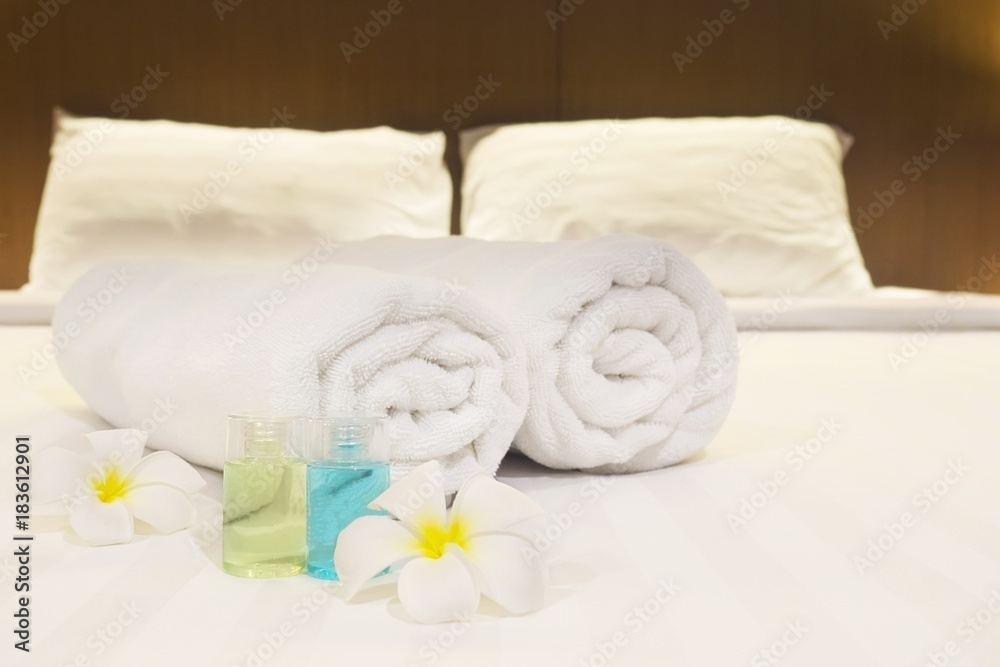 Hotel towel with flower and shampoo and soap bottle set on white bed Hotel towel with flower and shampoo and soap bottle set on white bed