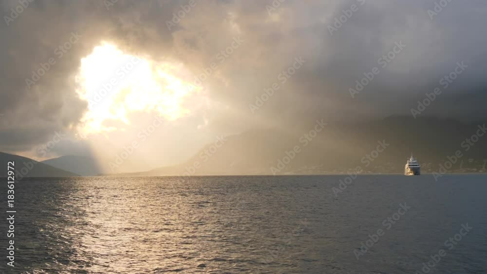 Cruise ship floats in rays of sunset light shining through break in stormy clouds Cruise ship floats in rays of sunset light shining through break in stormy clouds