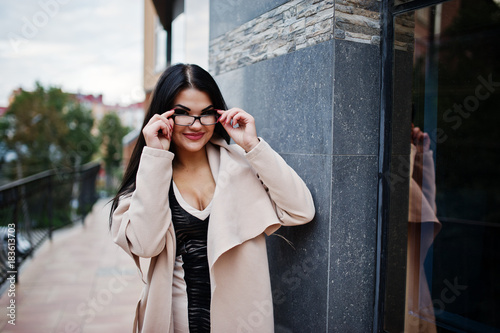 Black hair sexy woman in glasses and coat posed against building with modern windows. © AS Photo Family