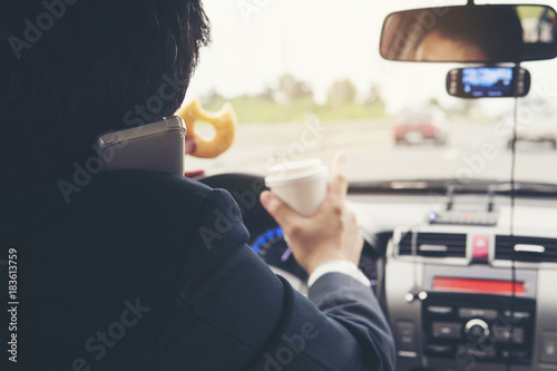 Man eating donuts with coffee while using mobile and driving car - multitasking unsafe driving concept