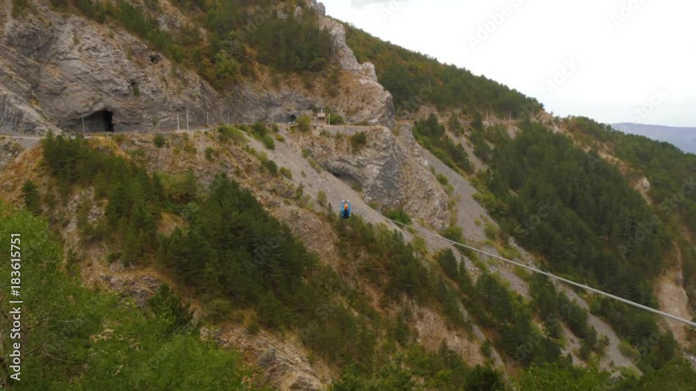 Zip-line in mountains. Man helps a woman to lounch pushing her for higher speed Zip-line in mountains. Man helps a woman to lounch pushing her for higher speed