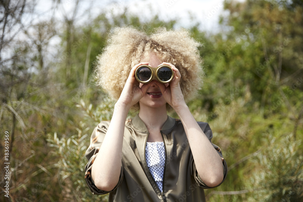 Young woman with curly hair looking through old binoculars Young woman with curly hair looking through old binoculars