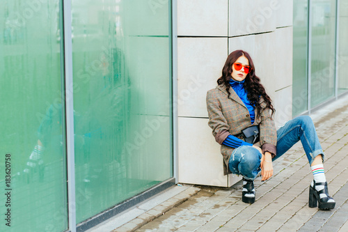 Stylish attractive young woman in red spectacles and torn jeans with black makeup posing squating photo
