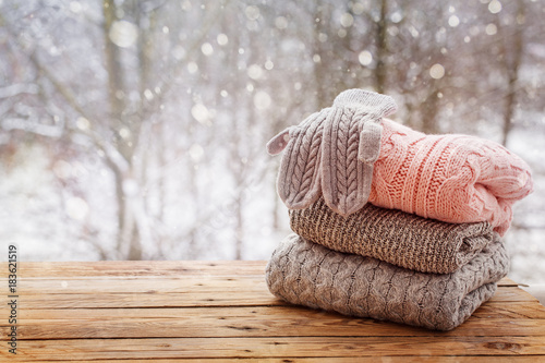 Stack of knitted clothes on wooden tableon winter nature background.