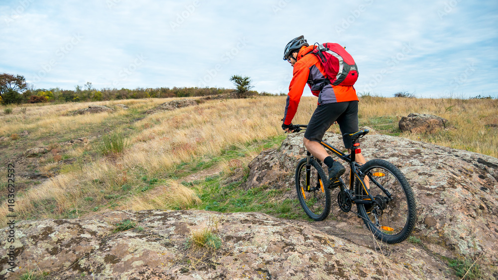 Cyclist in Red Riding the Mountain Bike on Autumn Rocky Trail. Extreme Sport and Enduro Biking Concept. Cyclist in Red Riding the Mountain Bike on Autumn Rocky Trail. Extreme Sport and Enduro Biking Concept.
