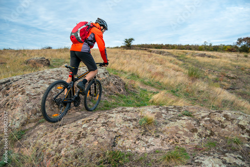 Cyclist in Red Riding the Mountain Bike on Autumn Rocky Trail. Extreme Sport and Enduro Biking Concept.