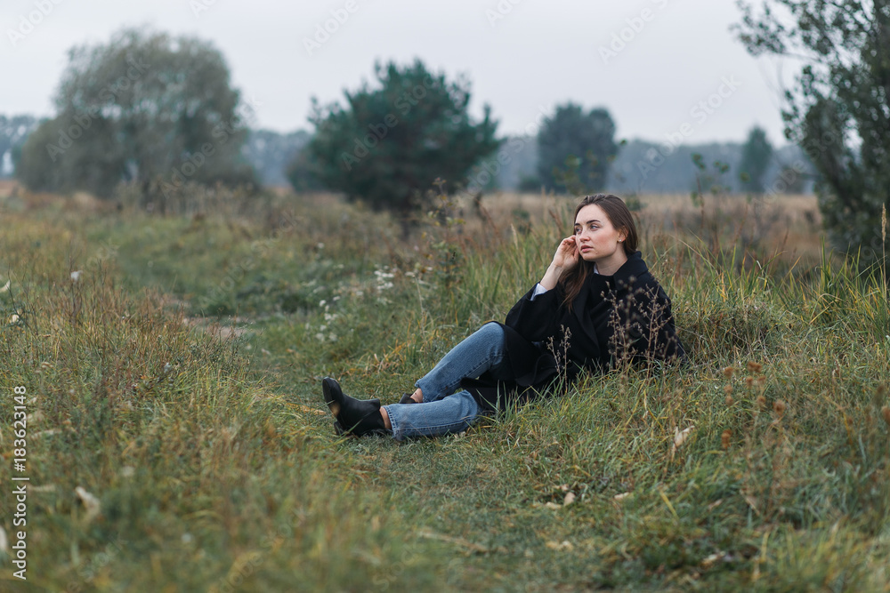 Brunette woman lying on dark green autumn grass. Casual fashion style Brunette woman lying on dark green autumn grass. Casual fashion style