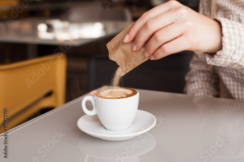 Young woman adding sugar in coffee