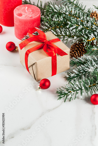 Christmas background for greeting card. Christmas tree branches with snow effect with festive red ribbon  pine cones  gift boxes and candles  on white marble background  copy space