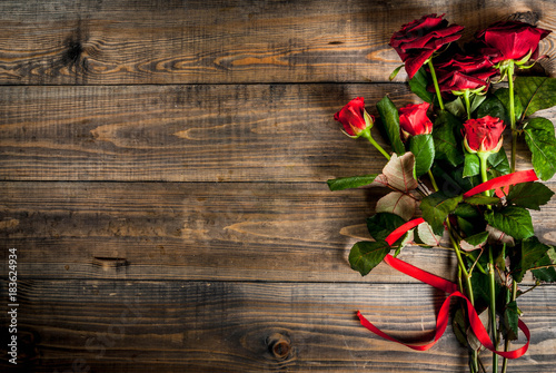 Holiday background, Valentine's day. Bouquet of red roses, tie with a red ribbon. On a wooden table, top view copy space