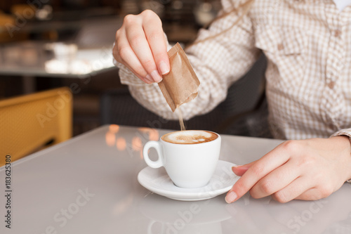 Young woman adding sugar in coffee