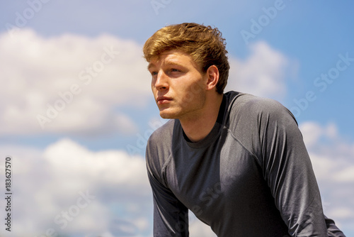 Young man resting after excercise on sunny day over sky with clouds.