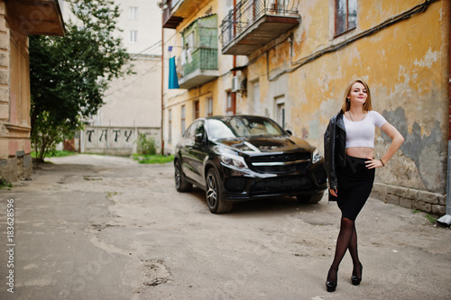 Elegant blonde girl wear on black leather jacket posing at streets of town background luxury car. © AS Photo Family