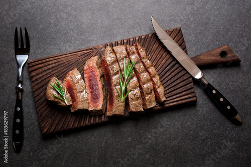 Rare steak on cutting board with rosemary and spices. Grilled beef steak top view