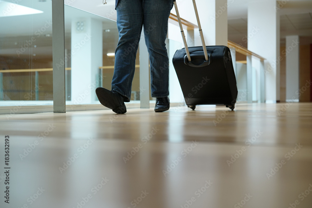 Fototapeta premium Closeup of traveller pulling suitcase in airport corridor