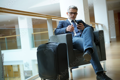 Businessman in airport waiting area connected with smartphone