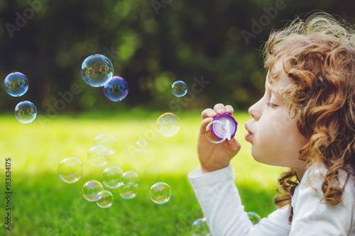 little girl blowing soap bubbles in summer park.
