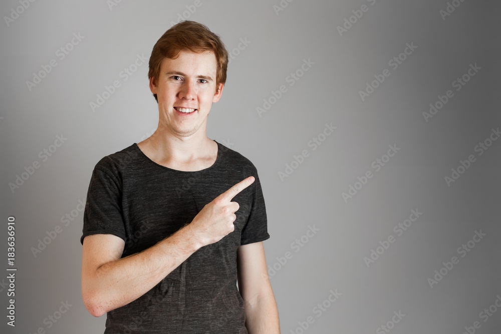Portrait of cheerful young redheads man smiling looking at camera pointing finger up. Over grey background. Copy space. Portrait of cheerful young redheads man smiling looking at camera pointing finger up. Over grey background. Copy space.