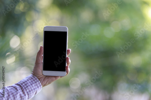 Hand holding smartphone with bokeh of trees