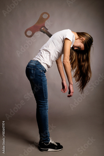 young woman with wind up  key in her back on a gray background