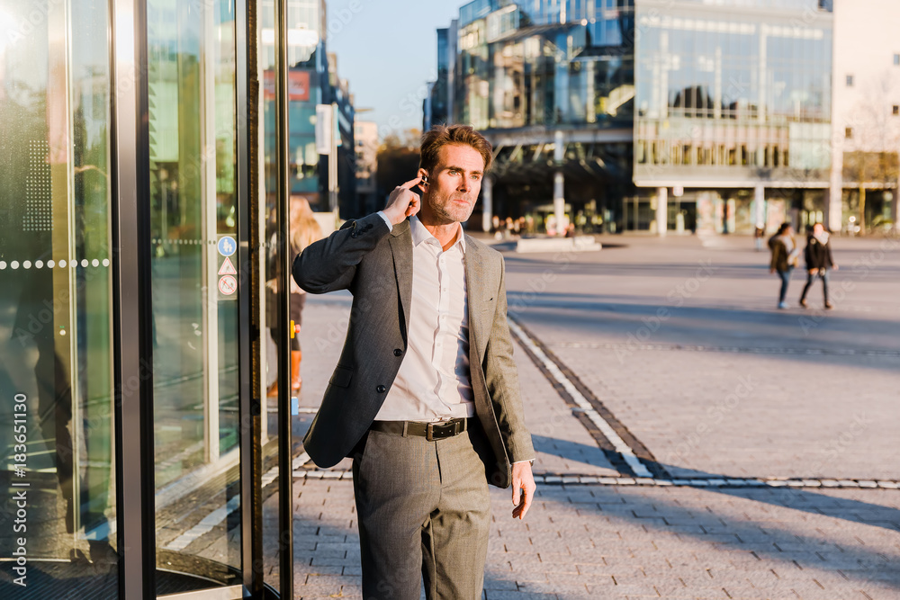 businessman with earphones comes out of an office building businessman with earphones comes out of an office building