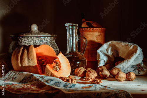 Rustic still life with pumpkin, walnuts, crockery  and vegetable oil in a bottle on a dark background