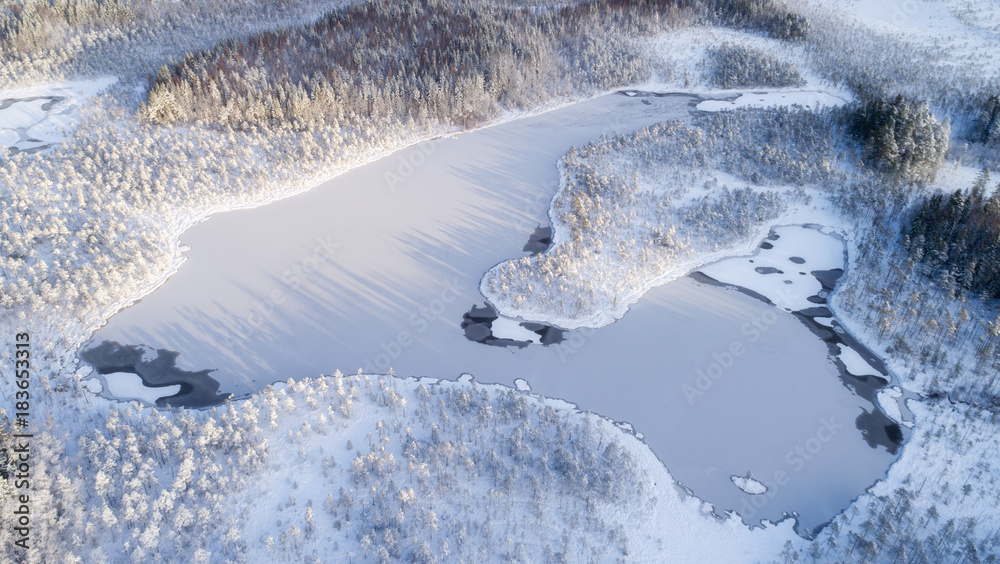Fototapeta Winter season aerial view of frozen lake in the middle of forest.