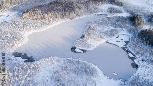 Winter season aerial view of frozen lake in the middle of forest.
