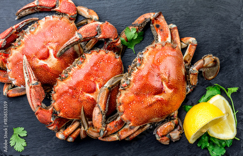 Cooked whole crabs on black plate served with white wine, black slate background, top view
