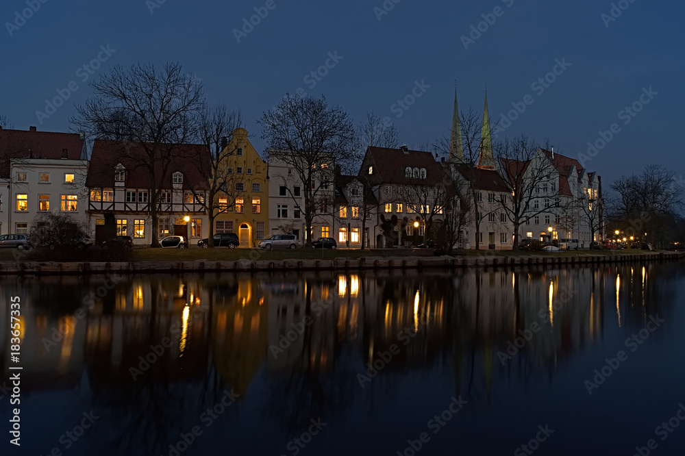 Row of houses with many lights on the riverbank with reflection at the blue hour