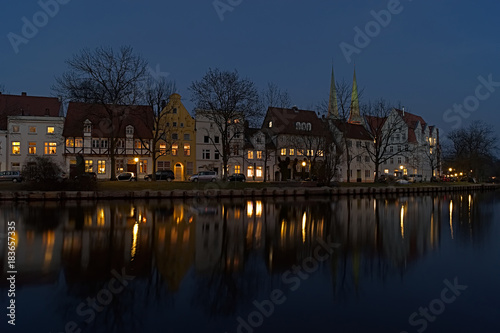 Row of houses with many lights on the riverbank with reflection at the blue hour