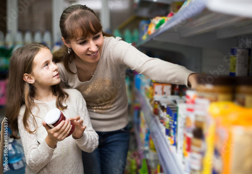 female with daughter choosing canned goods in food store