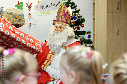 Święty Mikołaj rozdaje prezenty dzieciom w przedszkolu.
