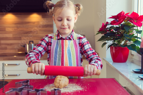 Pretty little girl with funny pigtails rolling dough for  christmas cookiess in kitchen photo