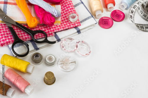 Multicolored threads, scissors, buttons, fabric and various sewing accessories on a light background with copy space flat lay