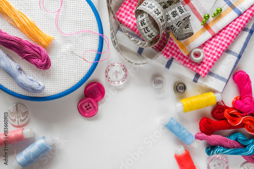 Multicolored threads, scissors, buttons, fabric, mulina, embroidery frame and various sewing accessories on a pink background with copy space © shintartanya