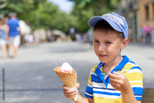 Cute European boy eating ice cream cone in a town street.