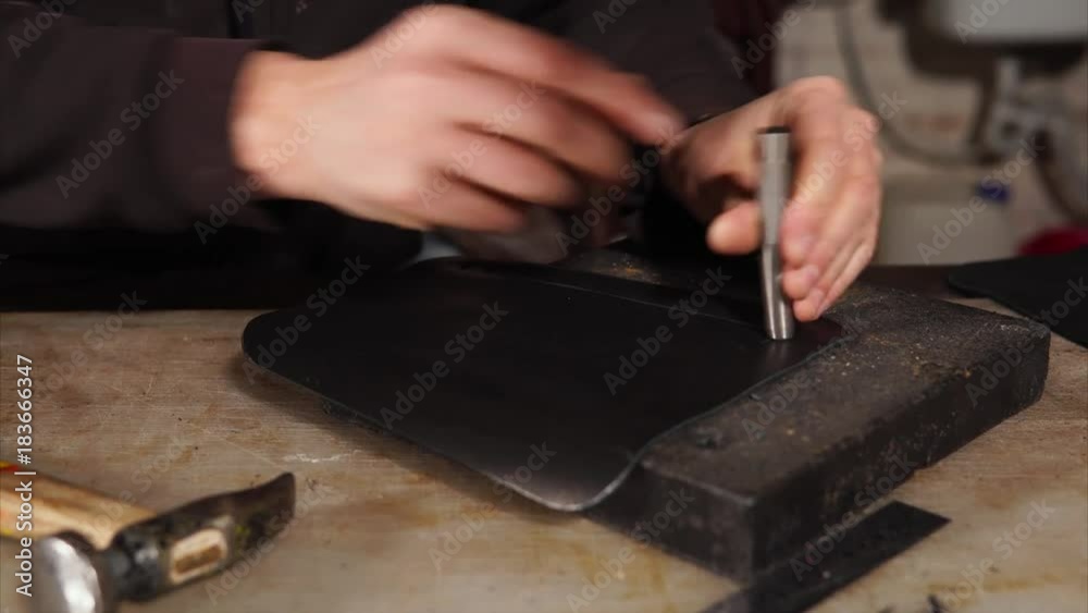 Close-up shot of a craftsman punching holes in leather detail. He using hammer and metal template Close-up shot of a craftsman punching holes in leather detail. He using hammer and metal template